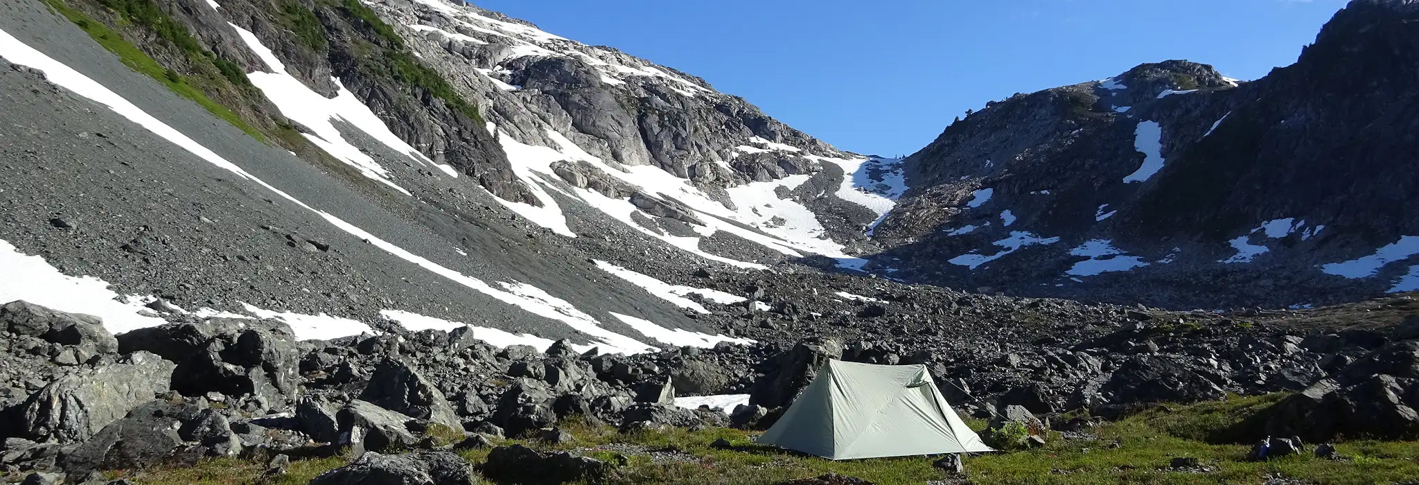 Backcountry camping tent among boulders surrounded by mountains, banner image.